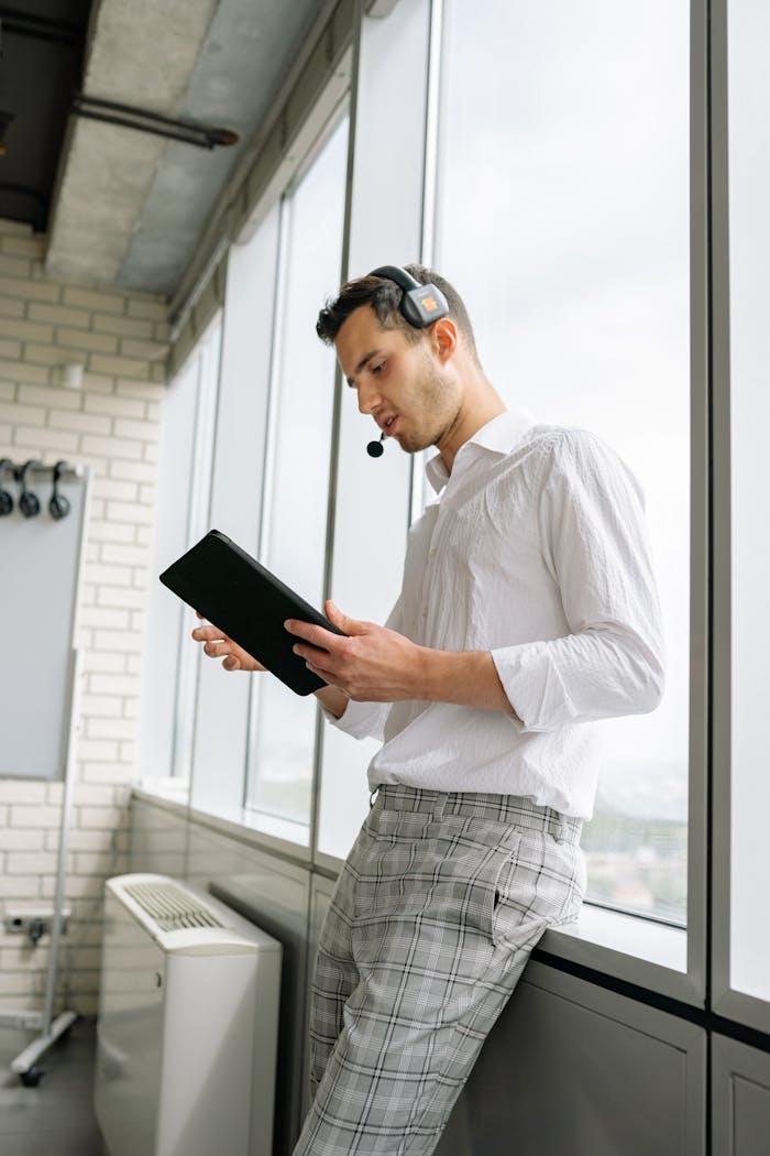 Focused call center agent using tablet by office window, wearing headset